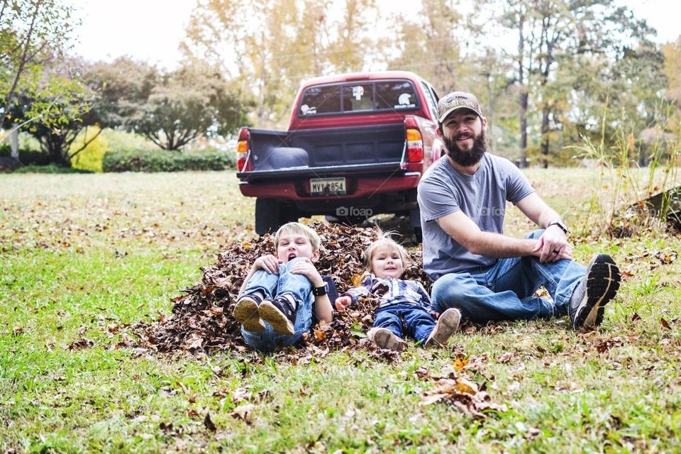 A dad and his 2 kids playing in a leave pile after doing yard work 