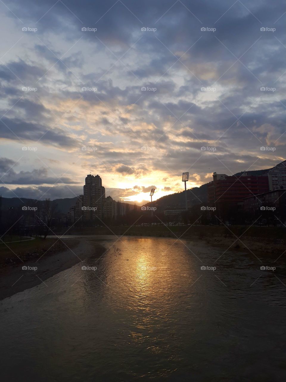 the sunset in my town, the sun sets between the famous apartment building on the Balkans Lamela building and reflector of the Bilino Polje stadium.the reflection is on a river Bosna.