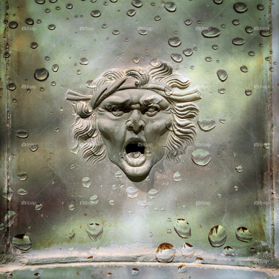 Angry face waterspout on an ancient Roman fountain 