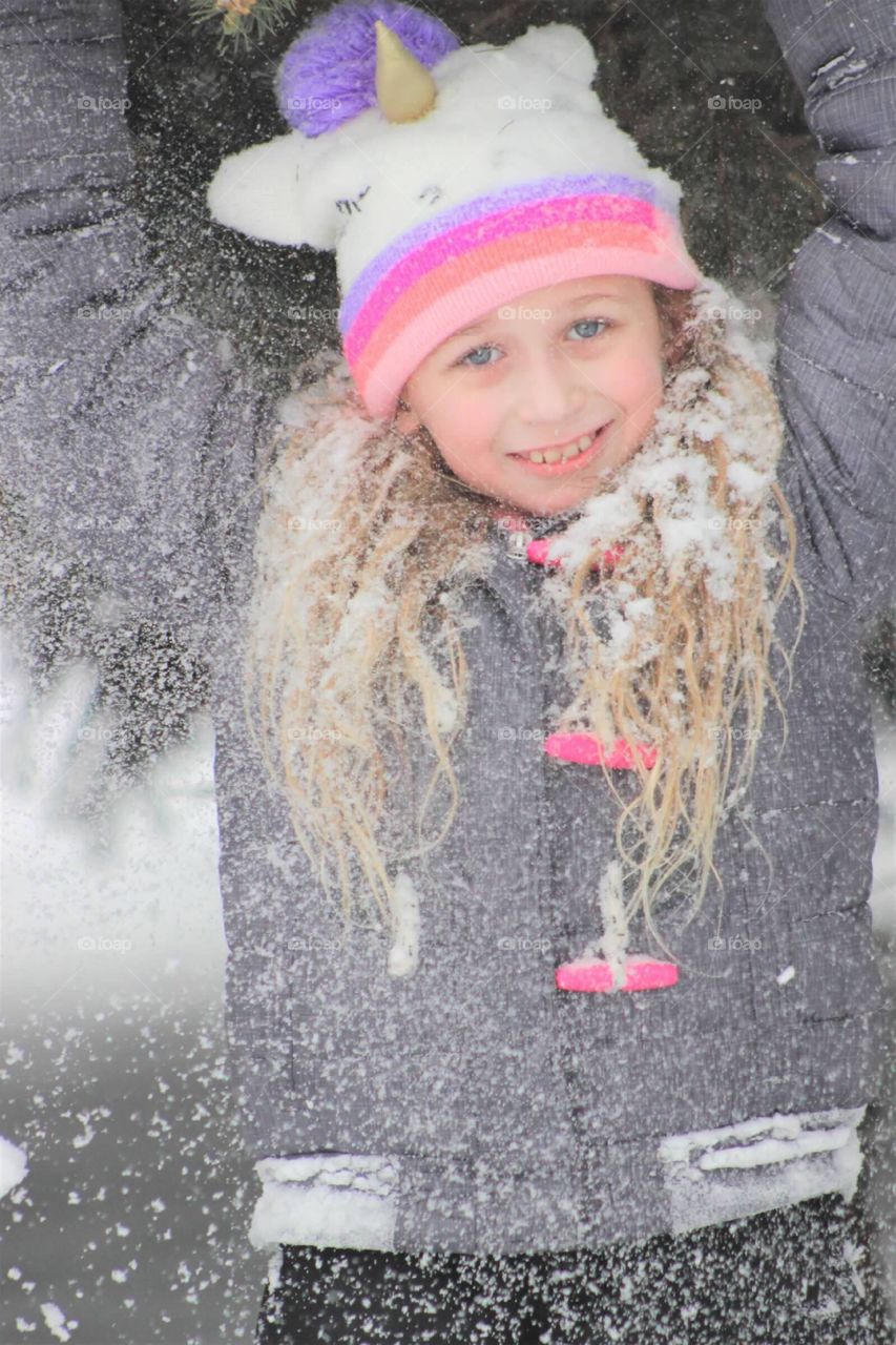 Playful little blue-eyed blonde haired girl covering herself in snow as she plays outdoors in winter. 