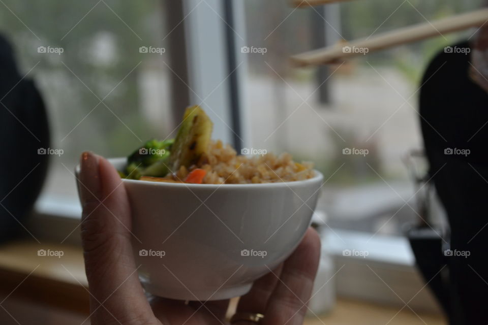 Woman's hand holding closeup bowl of Chinese fried rice using chopsticks 