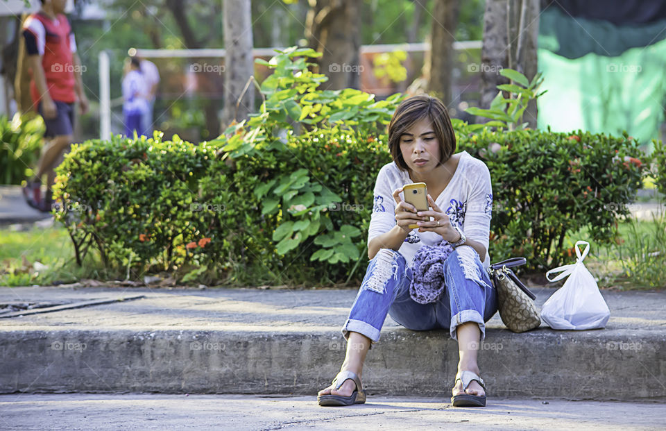 Asian women Sitting on the sidewalk along the street and play Mobile.