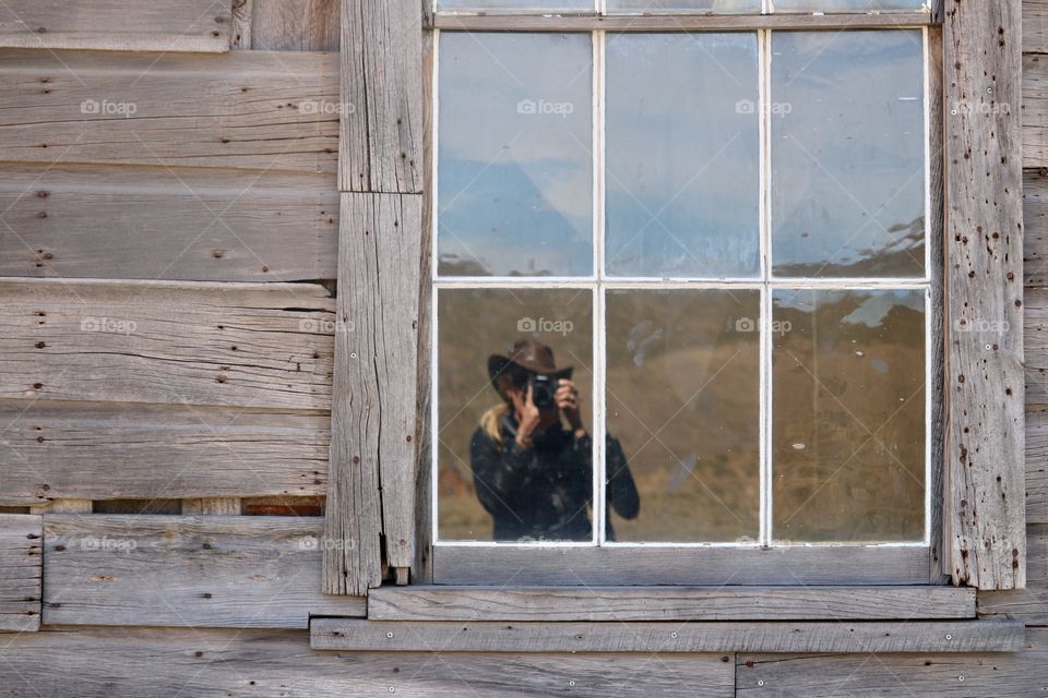 Reflection of female photographer in window of abandoned wood homestead in Nevada 