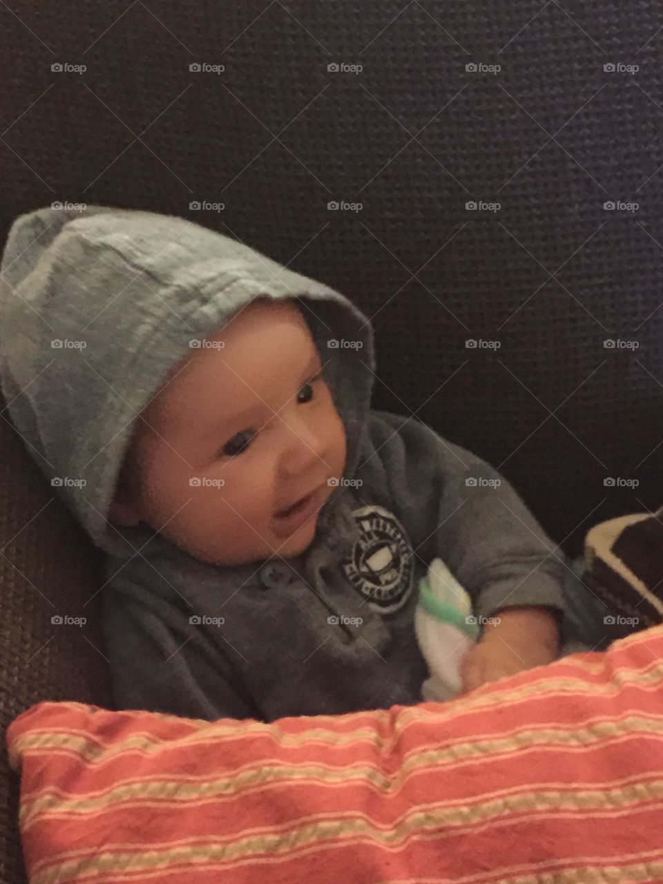 Two month old baby with a little hoodie on semi sitting on couch.