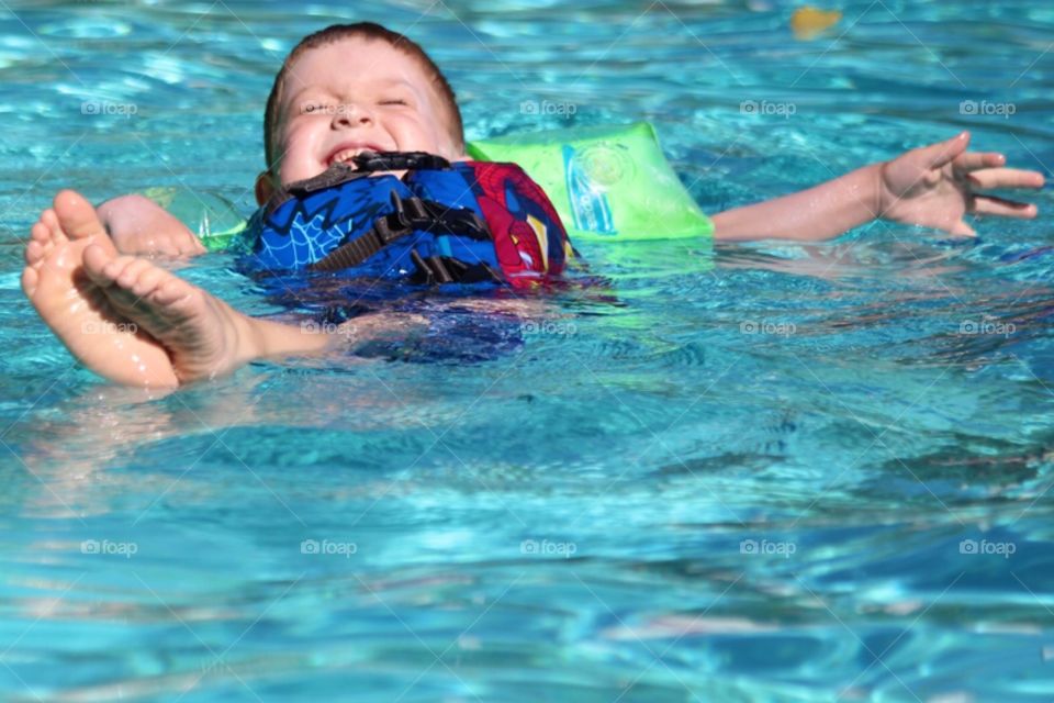 Little boy floating on water in swimming pool