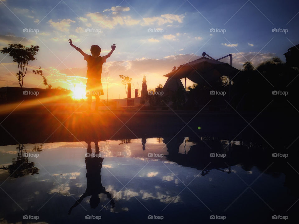 A victorious kid with hands up and a beauty sunset 