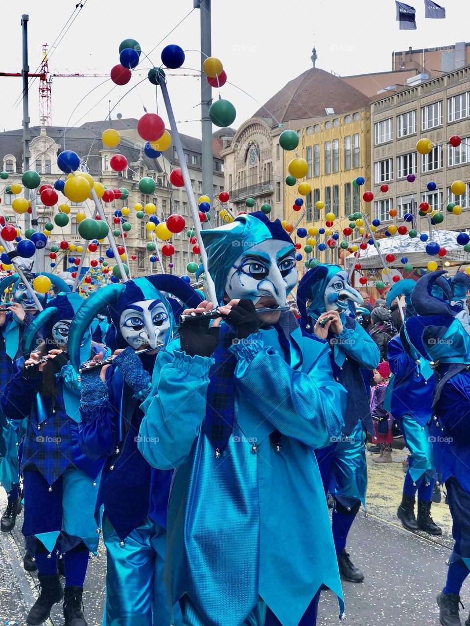 a large crowd of people running in the city among large buildings. a crowd of people in masquerade costumes and masks at a fundamental festival in Switzerland. people in bright costumes on a holiday