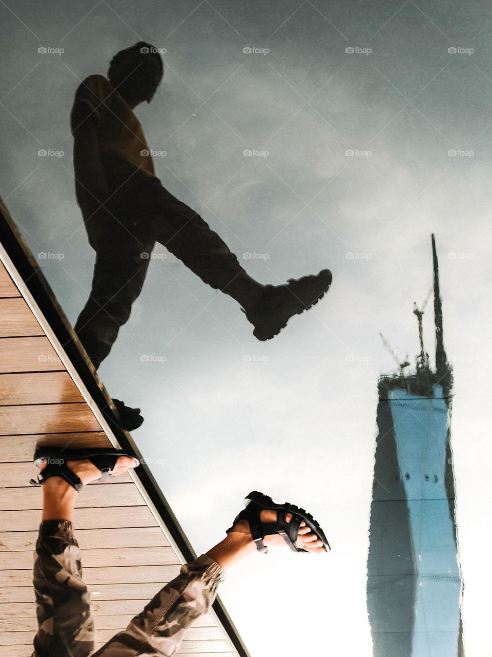 An upside down view of a man raising his feet above a calm pool of water with the world second tallest building in the background