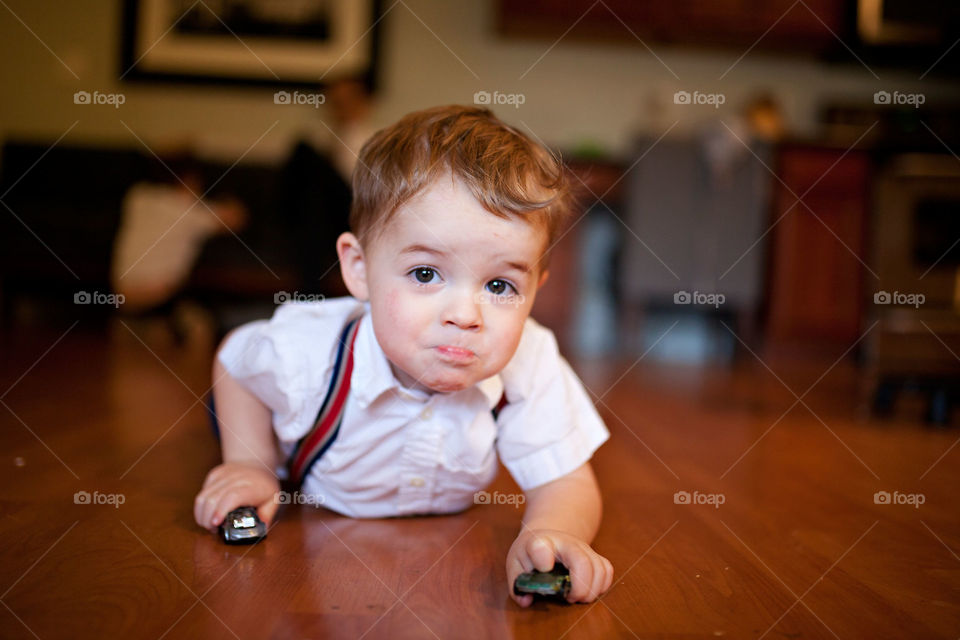 Toddler in suspenders and dress shirt driving matchbox cars on floor 