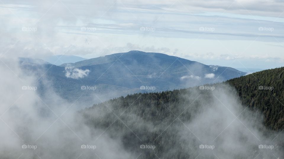 Beautiful view through the low foggy clouds to mountain range on top of mountain top summit