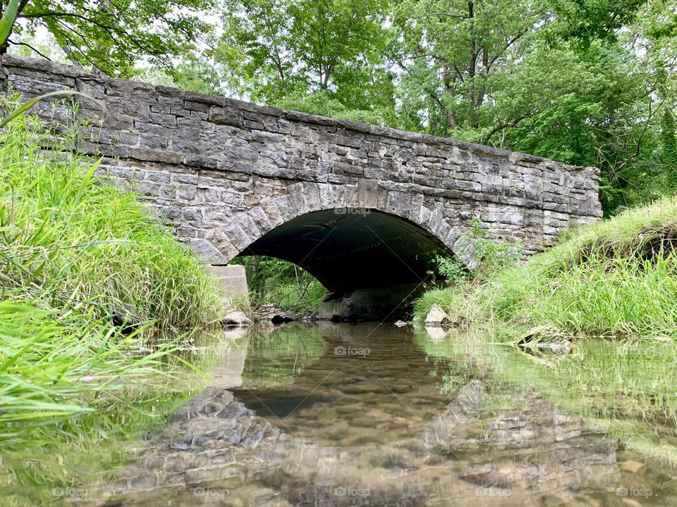 Side angle shot of a stone bridge with a gentle stream beneath it