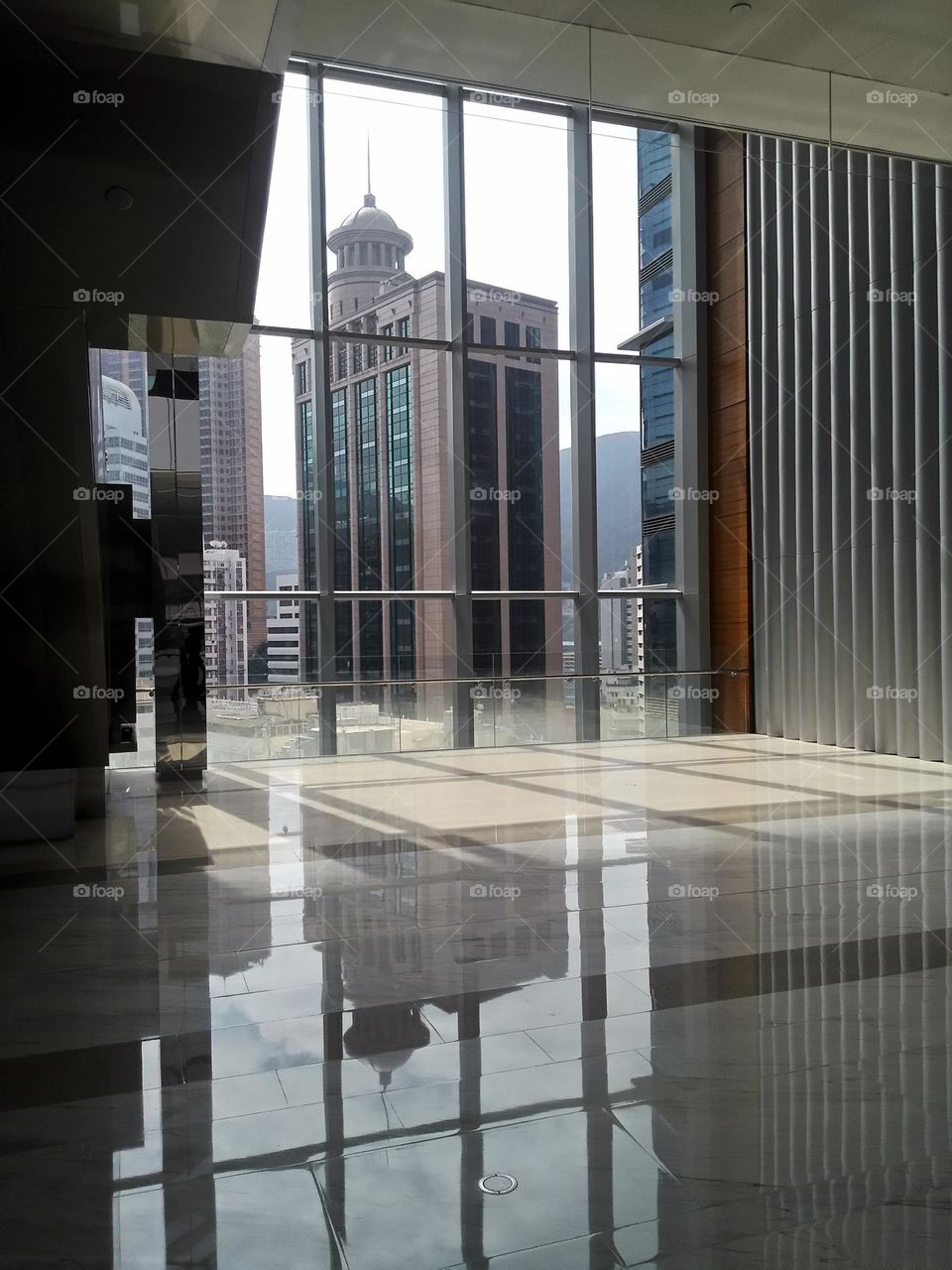 Buildings in Causeway Bay Hong Kong. Looking out Hysan Place large window at Lee Theatre Plaza, mirroring nearby buildings and having itself reflected on the floor of Hysan Place