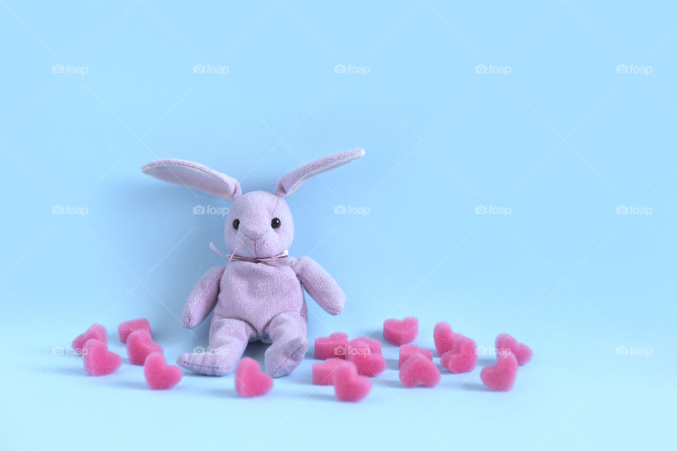 Pink toy rabbit is sitting next to pink hearts on the blue background. Love concept