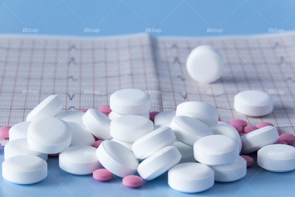 Pills and medicines lie on a blue background with an electrocardiogram of the heart.