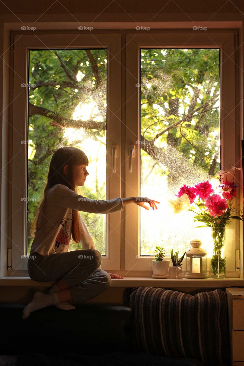 Little girl sits on a windowsill touches peonies