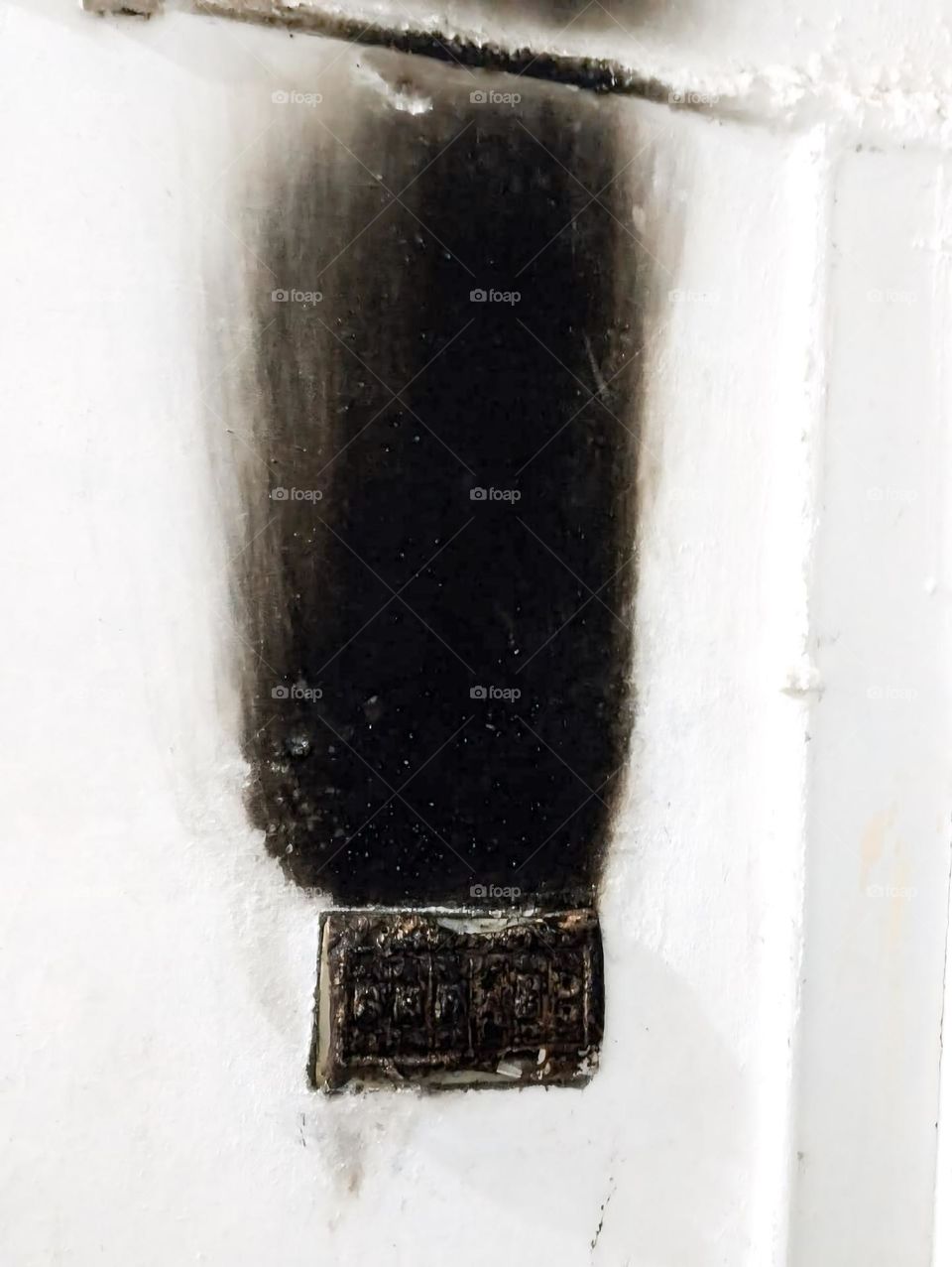 a heavily scorched or burnt section of a wall, likely caused by an electrical fire or malfunction. The black soot and charred area are concentrated around what seems to be an electrical outlet or switch box, indicating severe heat damage