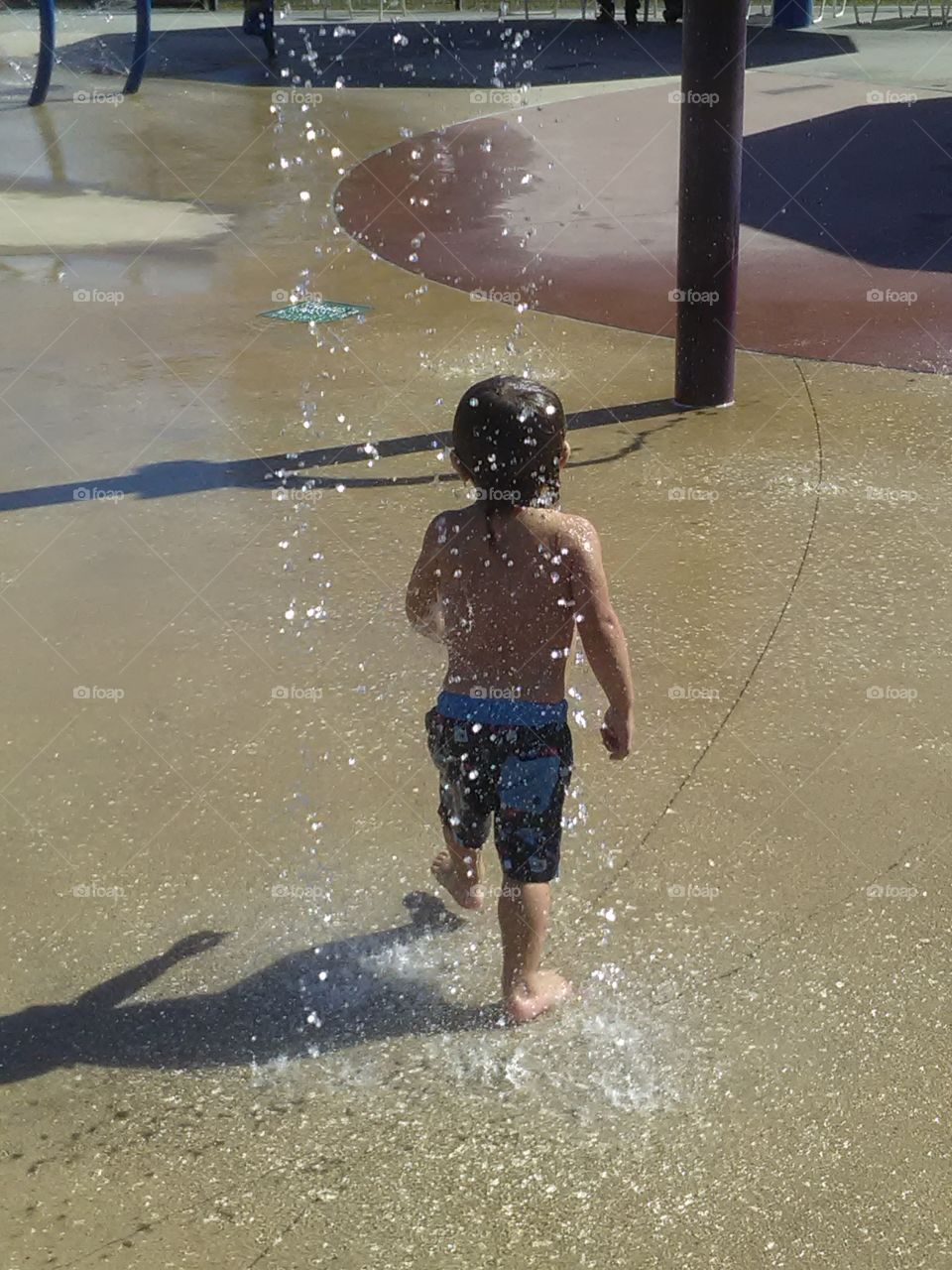 Rear view of boy having fun under water fountain
