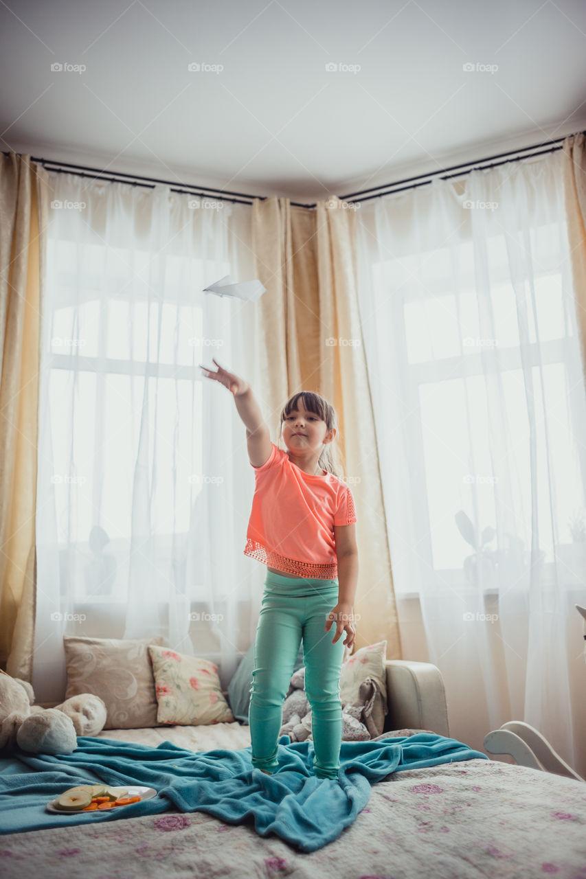 Little girl with paper plane on a bed 