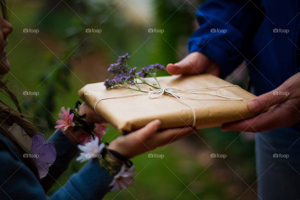 Sunny South African Christmas with flowers and outdoor festive fun. Image of gift wrapped in brown paper with flower. Little girl handing woman a gift.
