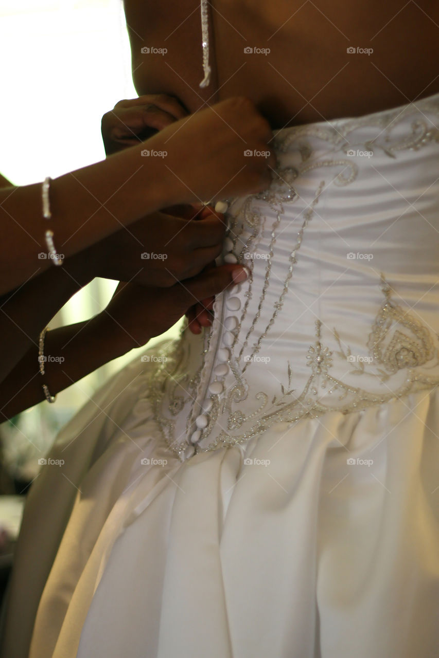 A bride is buttoned up from behind by her bridesmaids as she prepares to become a wife.