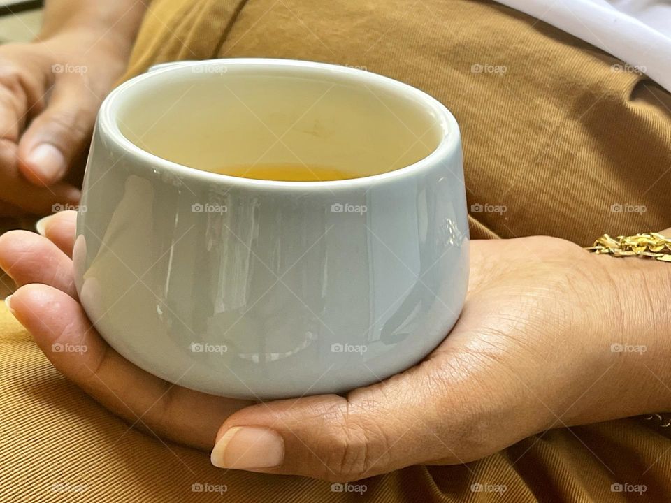 Women hand holding a ceramic pale blue painted cup filled with tea, relaxing time 