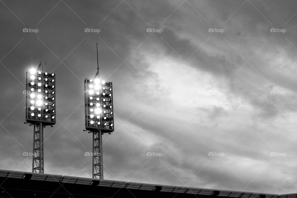 Black and white image of double baseball stadium lights illuminated at dusk