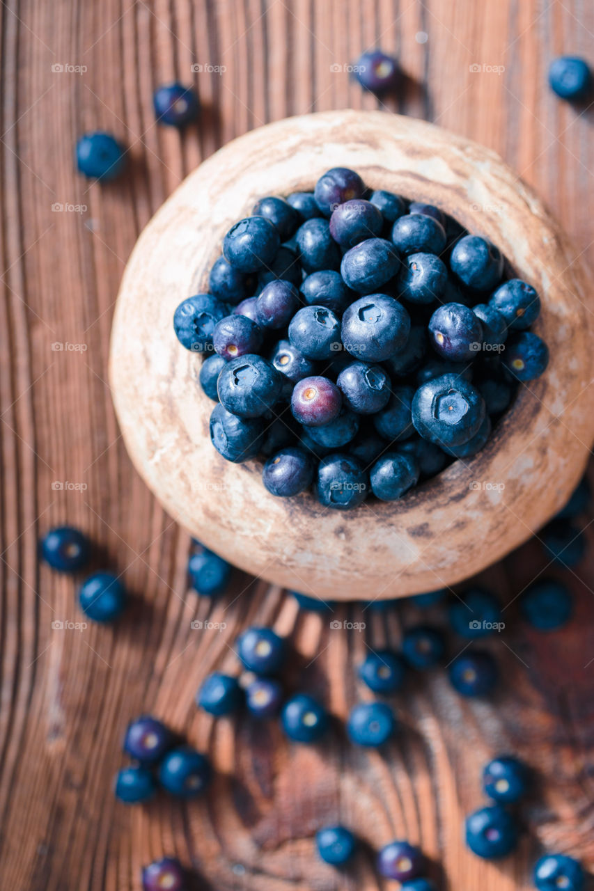 Freshly gathered blueberries put into old ceramic bowl. Some fruits freely scattered on old wooden table. Shot from above