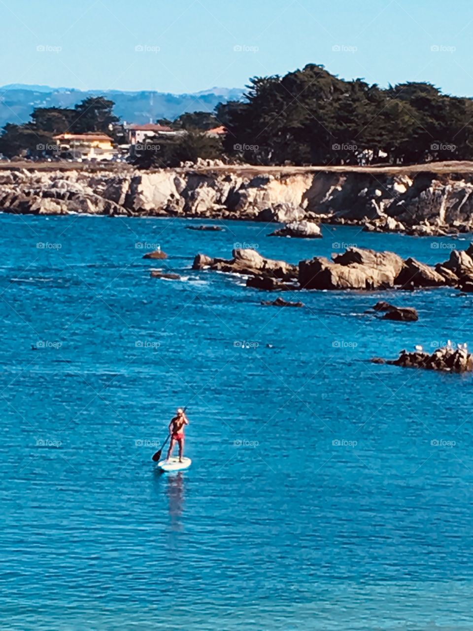 A man paddle-boards on the rich aqua blue Monterey Penninsula waters on a beautiful Monday afternoon. What a treasure to enjoy the inlet all on his own. 
