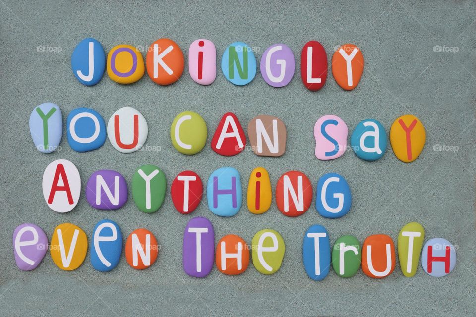 Jokingly you can say anything even the truth, creative quote text composed with multi colored stone letters over green sand