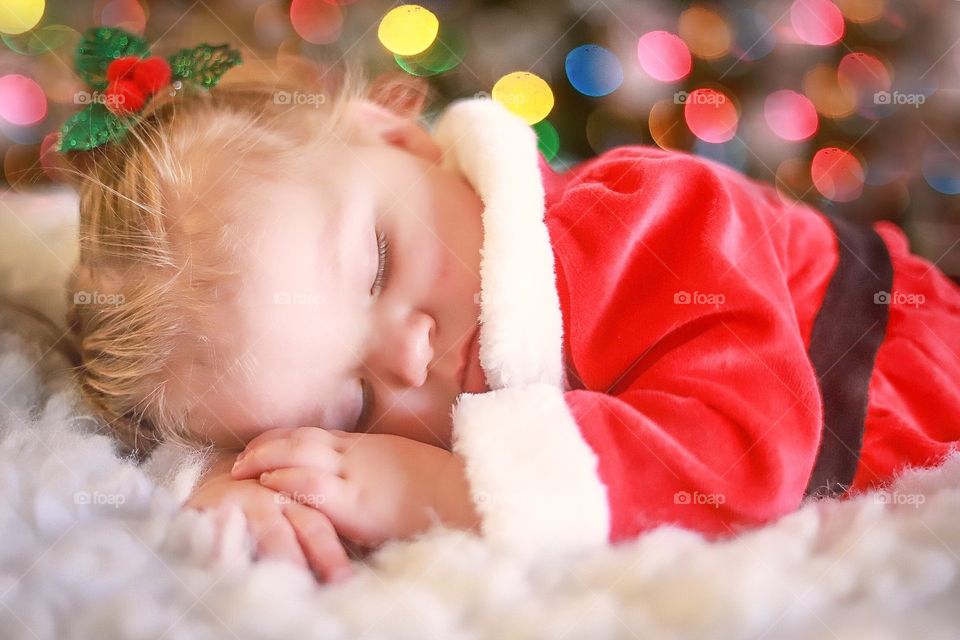 A little girl laying by the Christmas tree