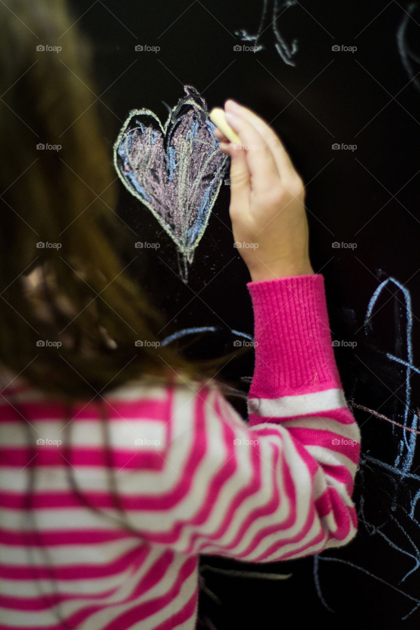 Art at home - girl drawing a heart on black board on the kitchen door at home.