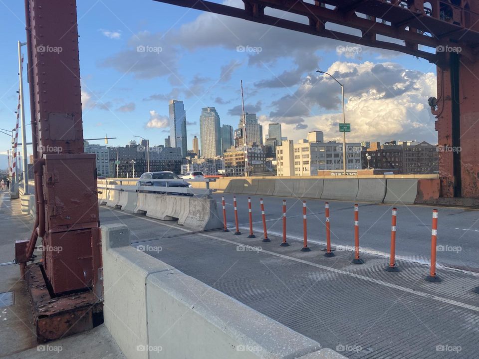The red metal arch of the “Pulaski Bridge” can be seen from the pedestrian lane and in the far distance the skyscrapers of “Long Island City”, Queens. 2023. Hypnotic Productions