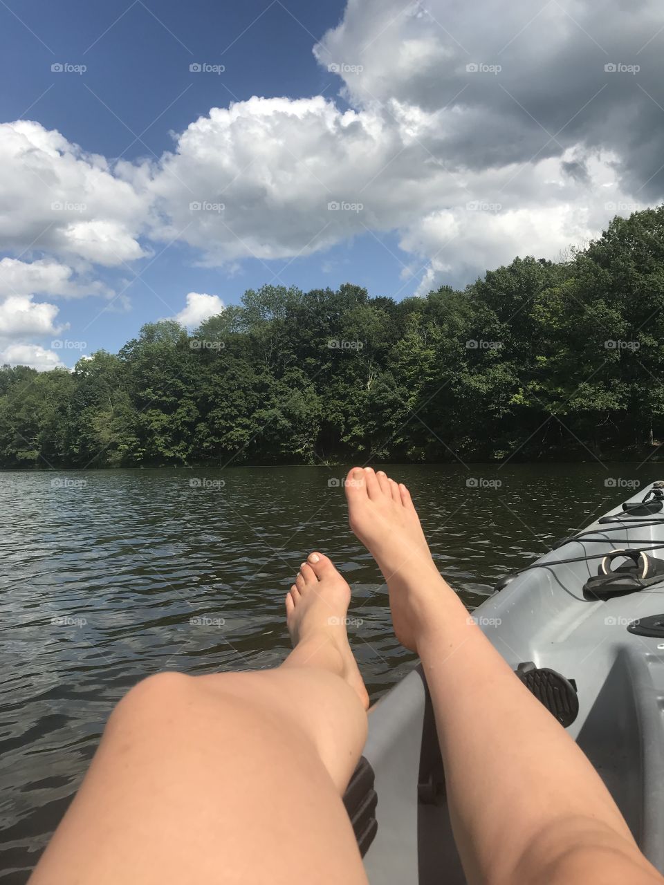 A pair of legs stretch out in a kayak. It is a beautiful day to rock on the small waves of a hidden New Jersey treasure. The ratio of scattered clouds and sun are just right for a comfortable day out on the lake. 