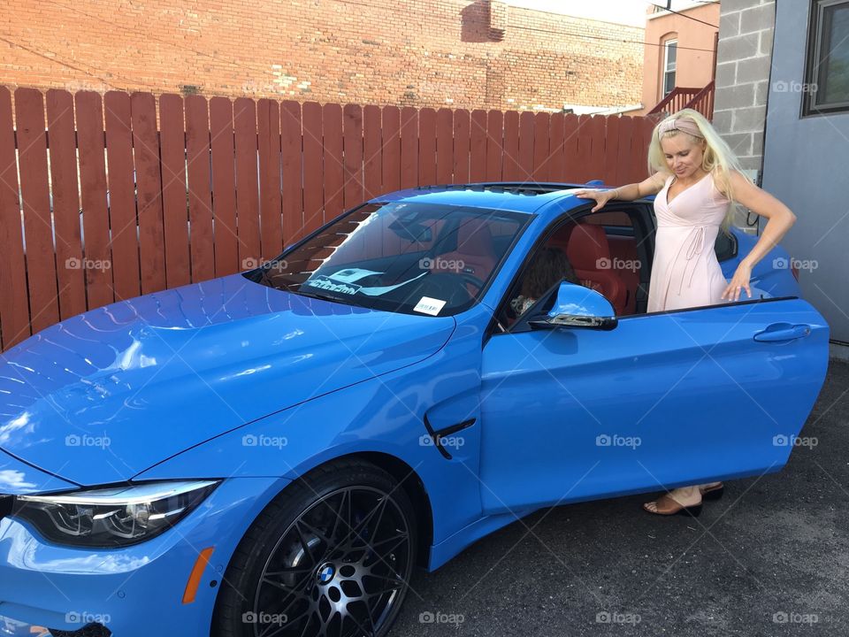 beautiful blonde woman getting into her new blue BMW sports car 
in the summer time
