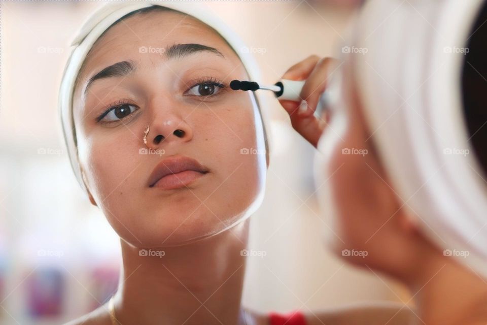 Pretty young woman is putting a mascara on her eye lashes
