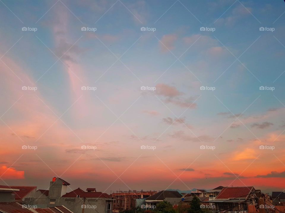 The view in the evening, before sunset, clouds refract red orenge yellow, the sky looks a little blue, its still a little bright, the residential light are still off, beautiful color view, beutiful clouds and sky,