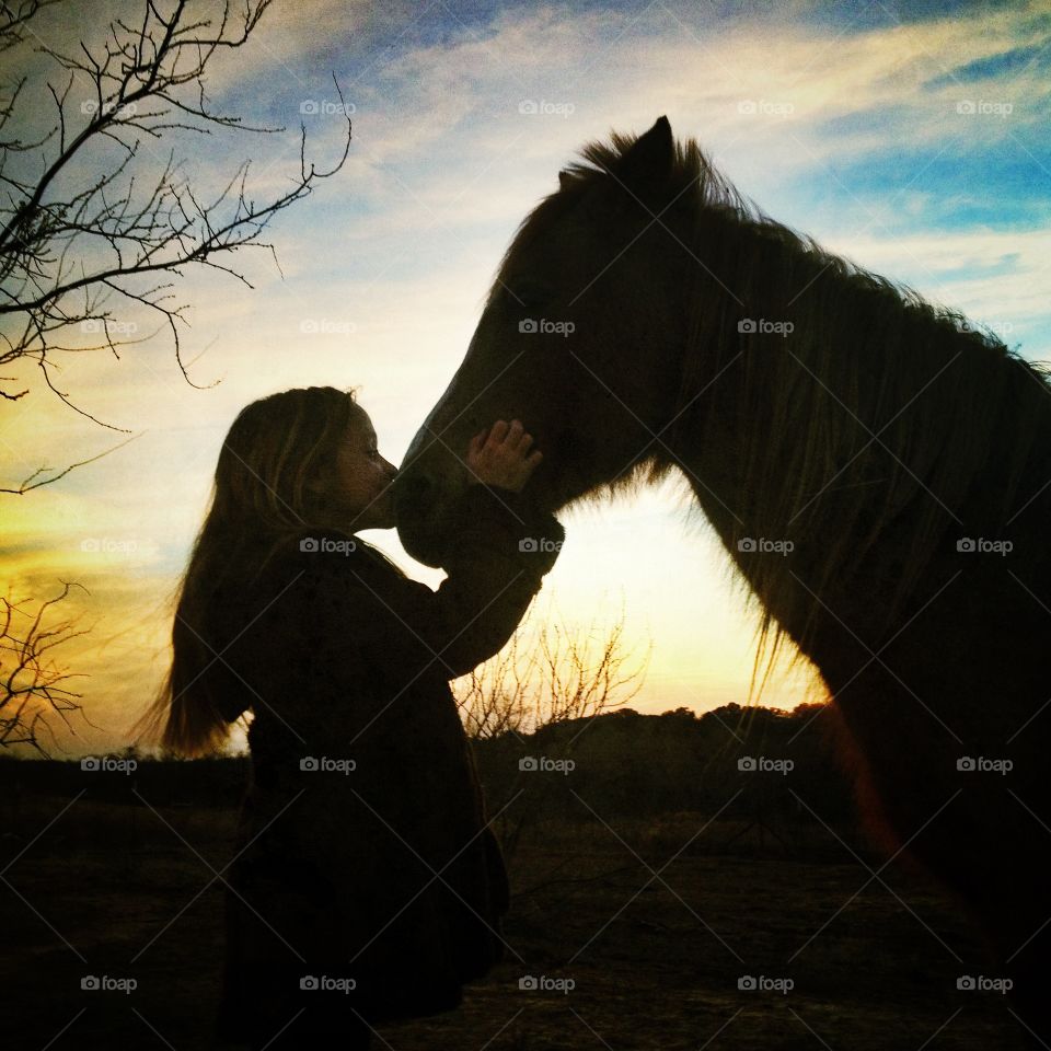 A girl and her pony in silhouette with sunset behind them