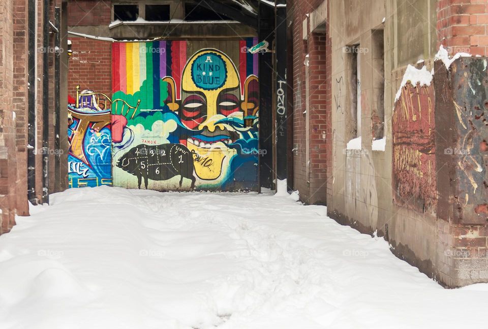 A snowy alleyway with a graffitied wall at the end