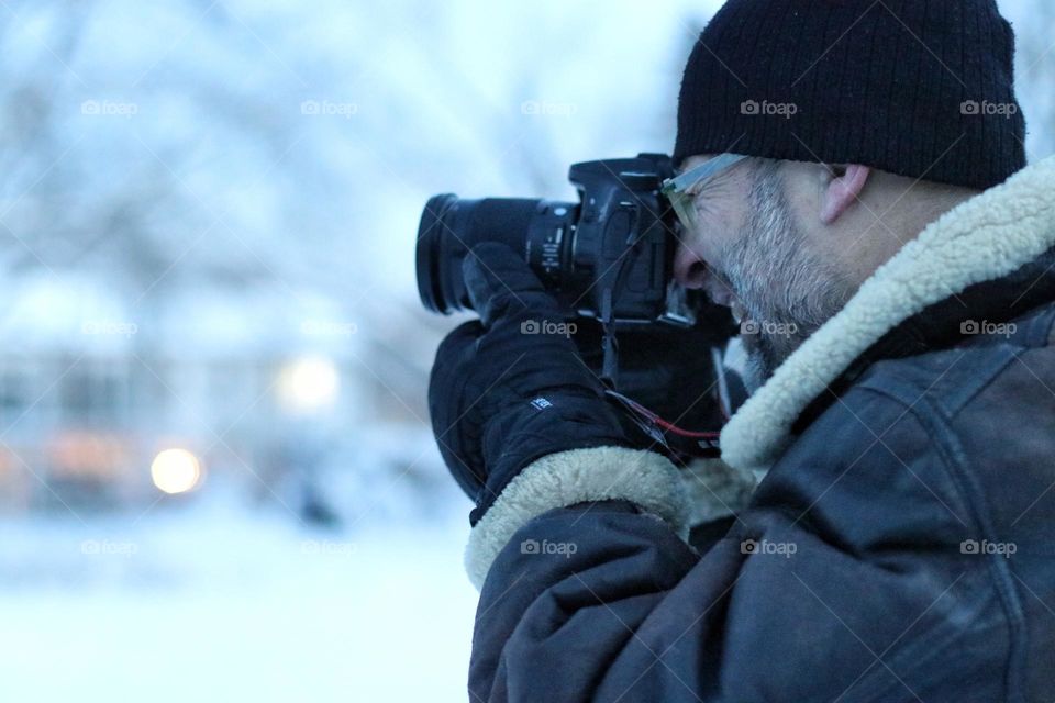 A man in winter clothing and gloves holds a digital camera in his hand and films in a white winter landscape