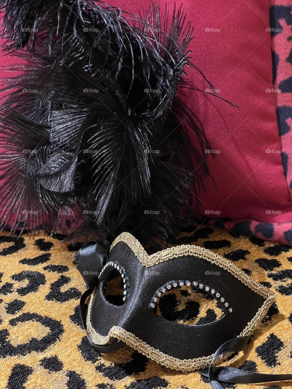 satin mask and black feathers on an animal and burgundy patterned background, carnival season, costumes and masks