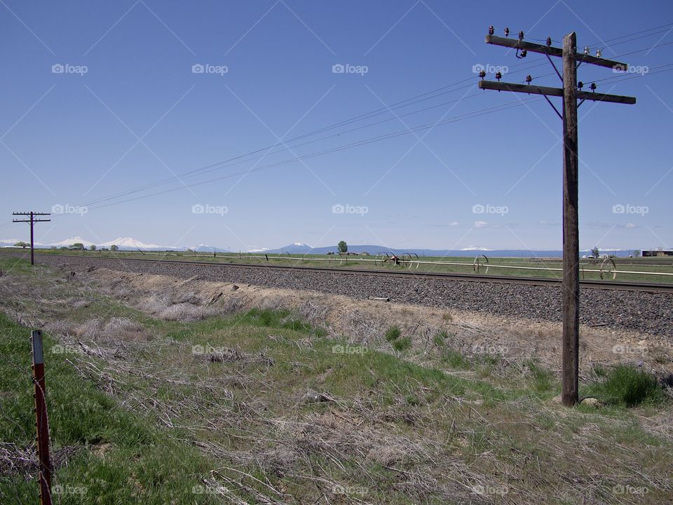 An old wooden telephone pole next to railroad tracks with the Cascade Mountains in the background on a beautiful sunny spring morning in rural Central Oregon. 