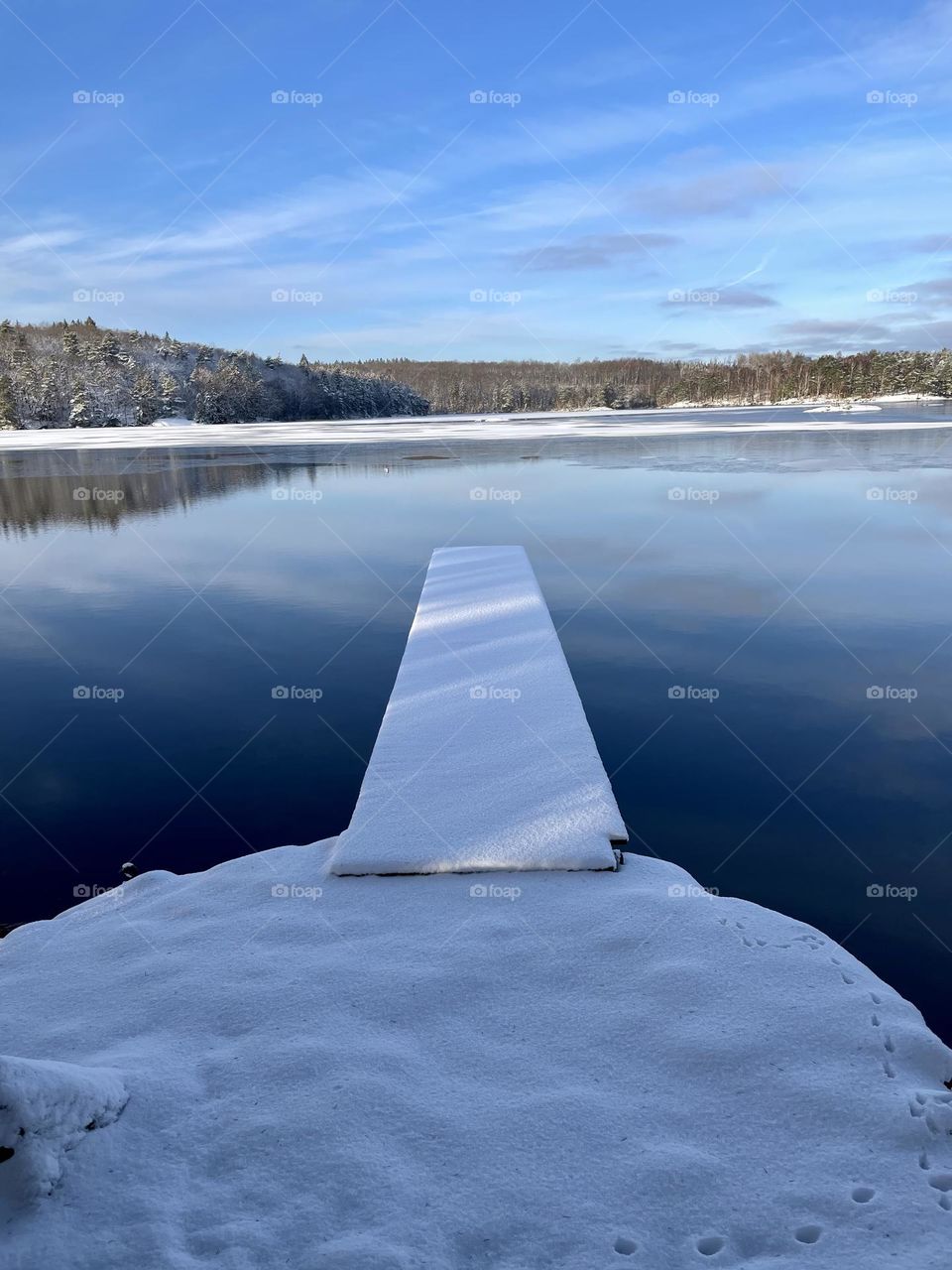 Snow covered wooden pier and reflection in calm peaceful lake water on a beautiful winter day 