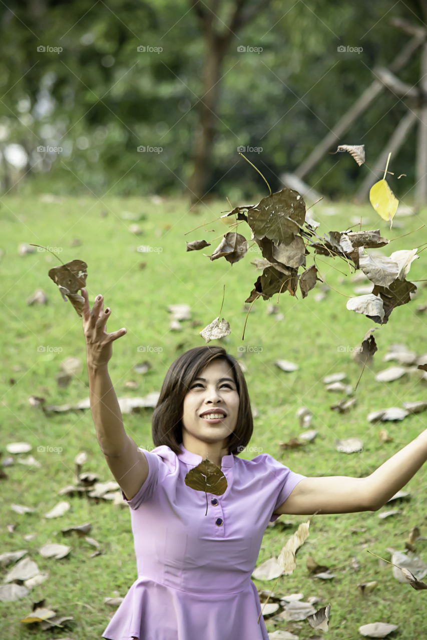 Portrait of Asean woman throwing dry leaves on the lawn in a park.