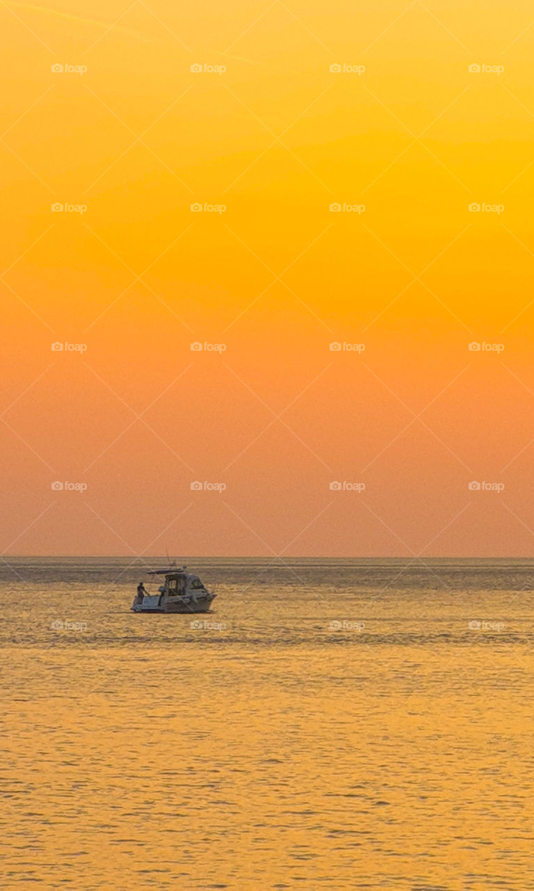 Summer seascape.  Bright orange sunset on the calm Adriatic Sea on which the boat floats.  Croatia, Dalmatia, Brela