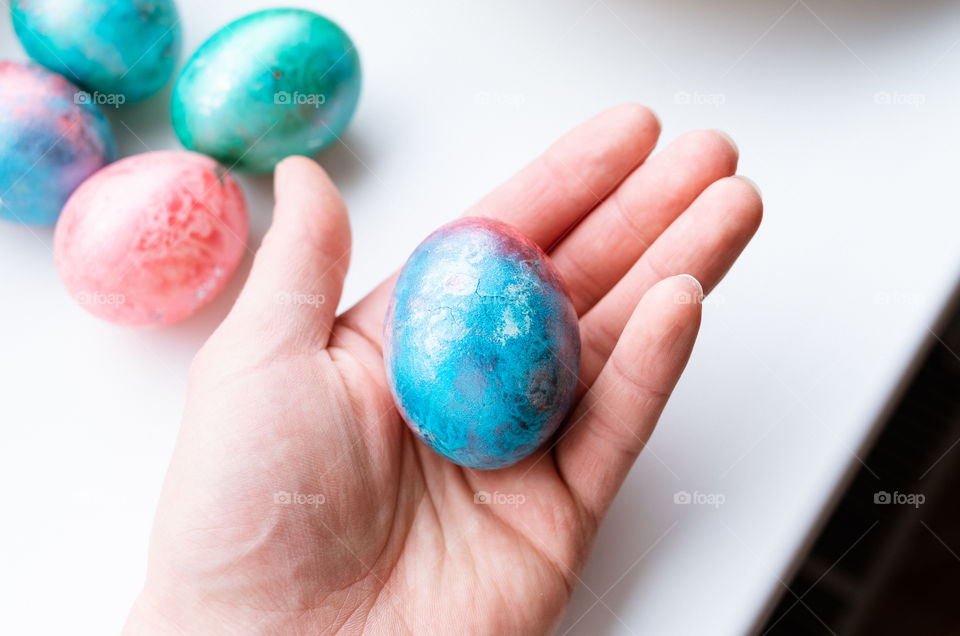 Top view of human hand holding a colourful dyed Easter egg on a white background.