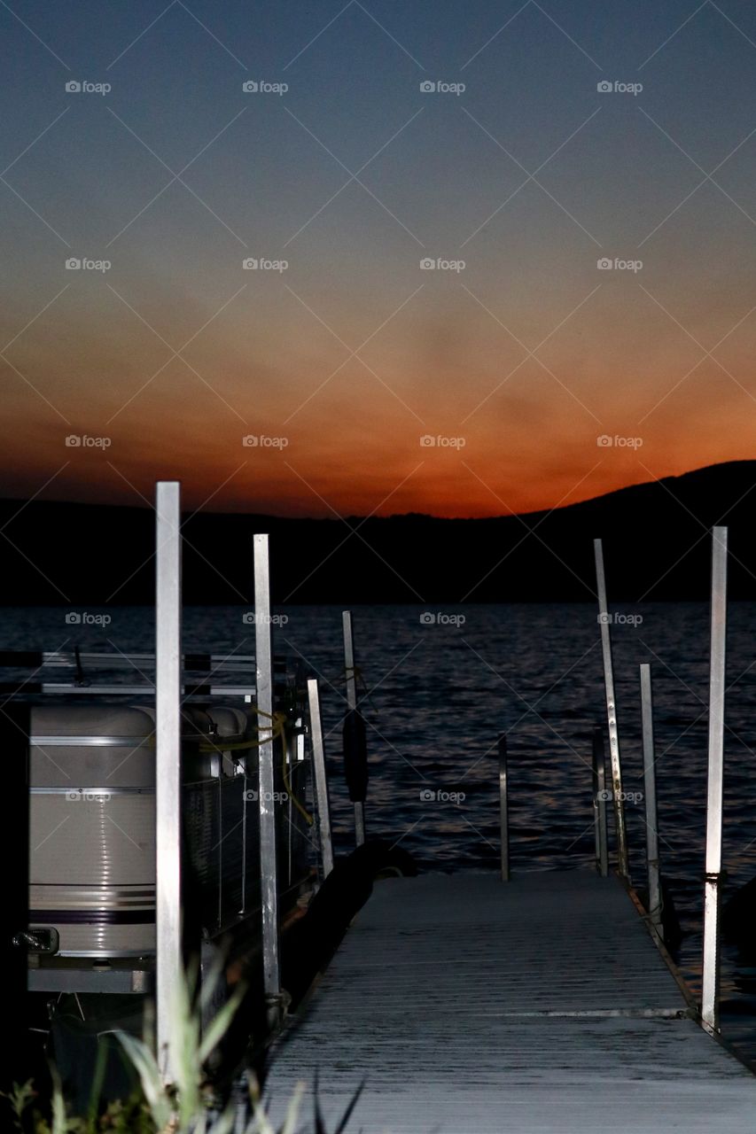 Boat tied to dock on lake at sunset 