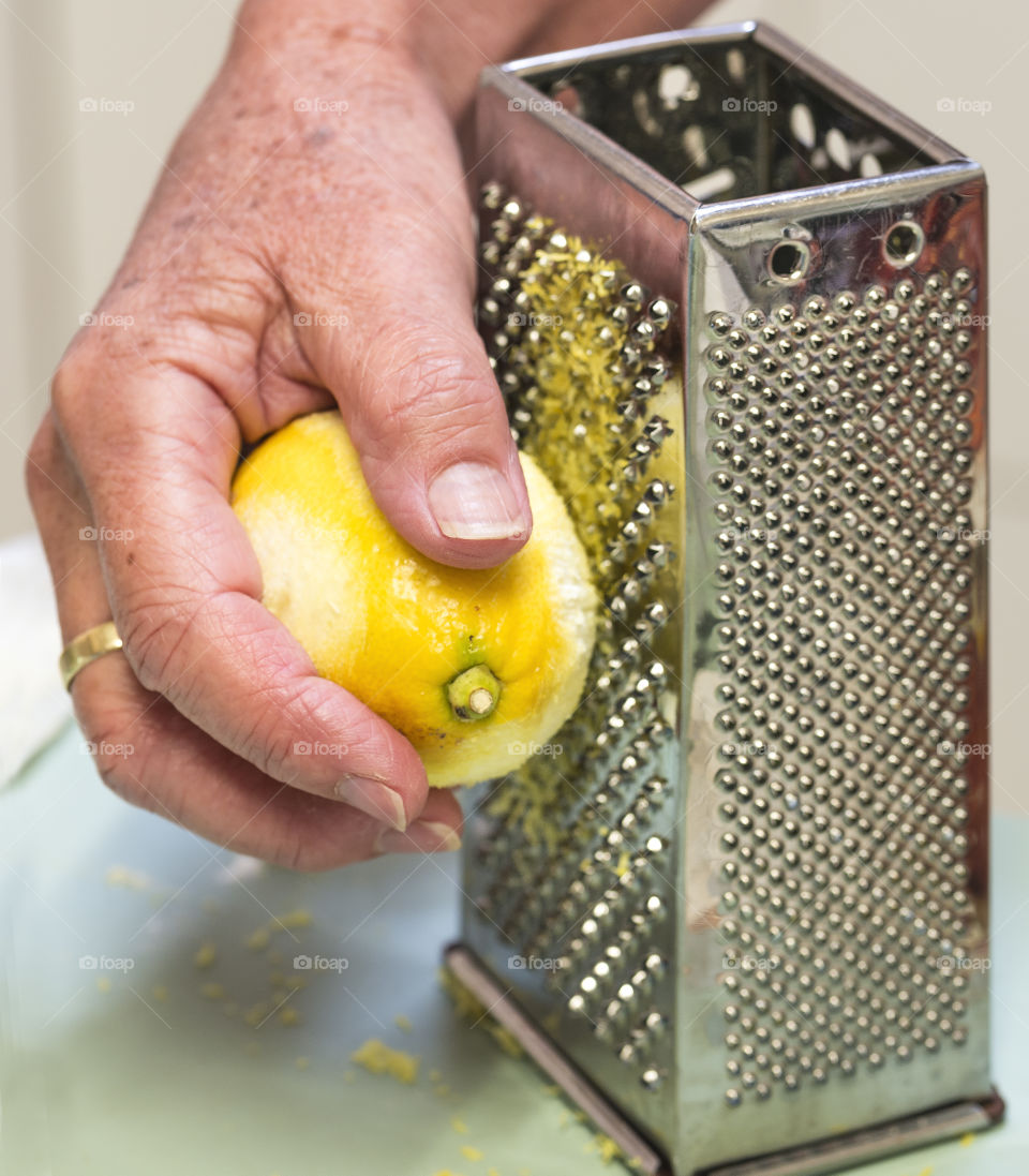 A woman's hand grates a lemon against  a metal grater.