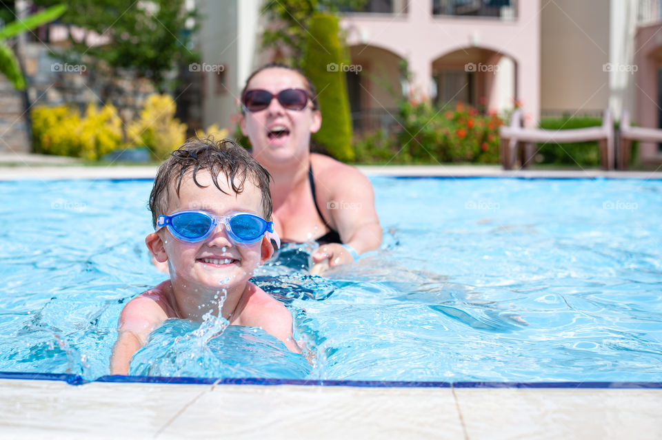 Happy small boy having fun playing with his mother in swimming pool.