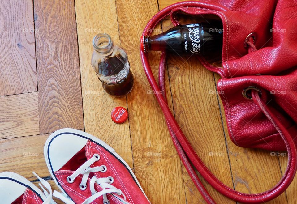 Coca Cola bottles on hardwood floor with red sneakers and red leather bag.