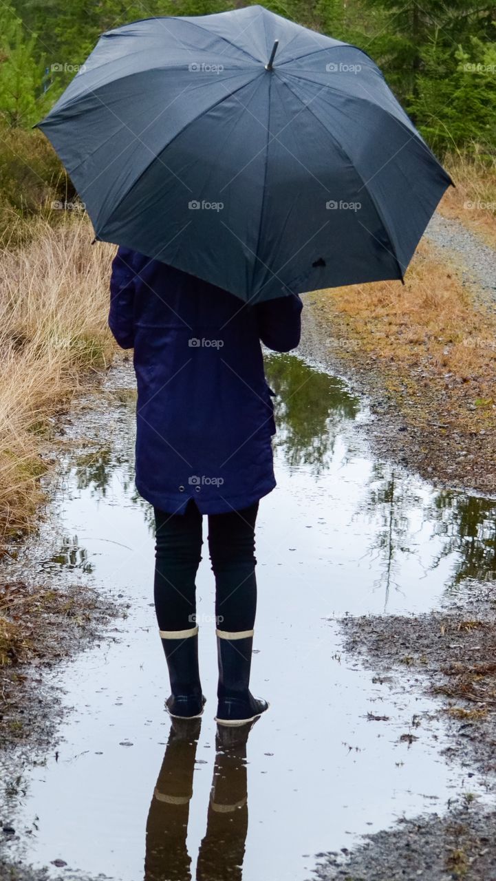 Rear view of a person holding a umbrella standing in a puddle